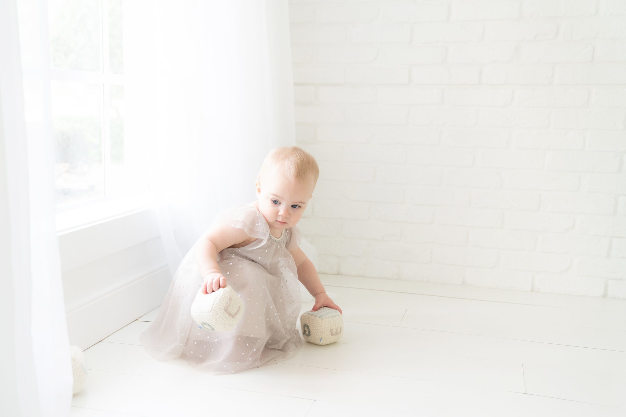 baby in a sparkly silver grey dress by large windows with white curtains jupiter florida photography studio