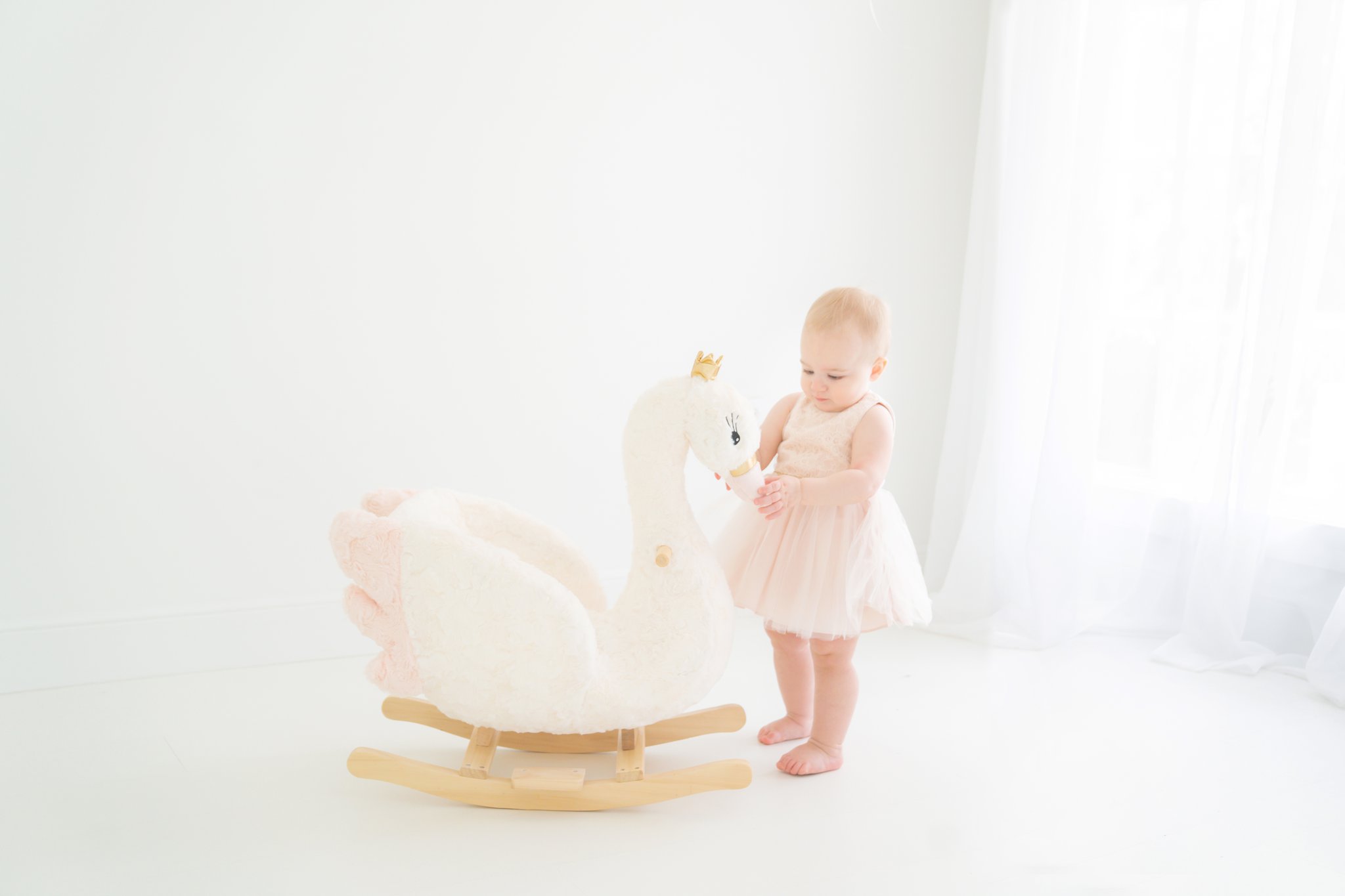 baby looking a a pretty stuffed swan rocker in jupiter florida photo studio