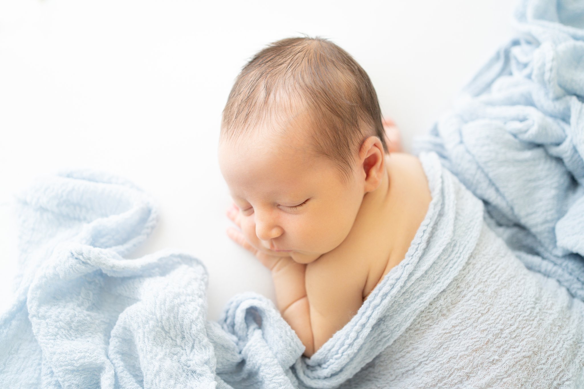 10 day old newborn baby posed and curled up asleep being photographed