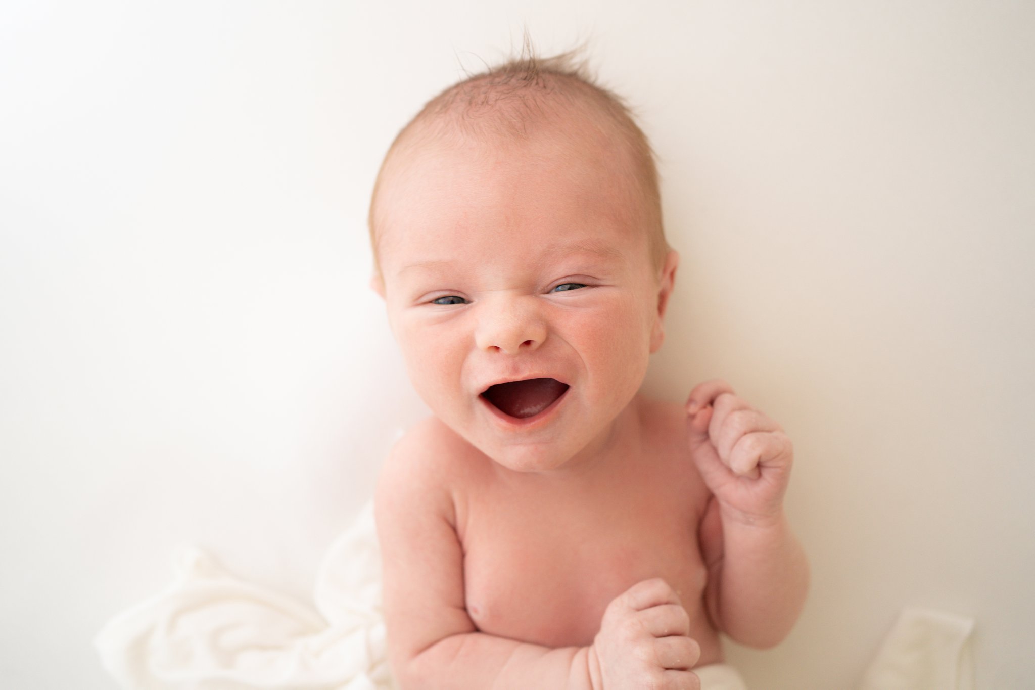 Newborn smiling at the photographer, laying on white backdrop in photography studio.