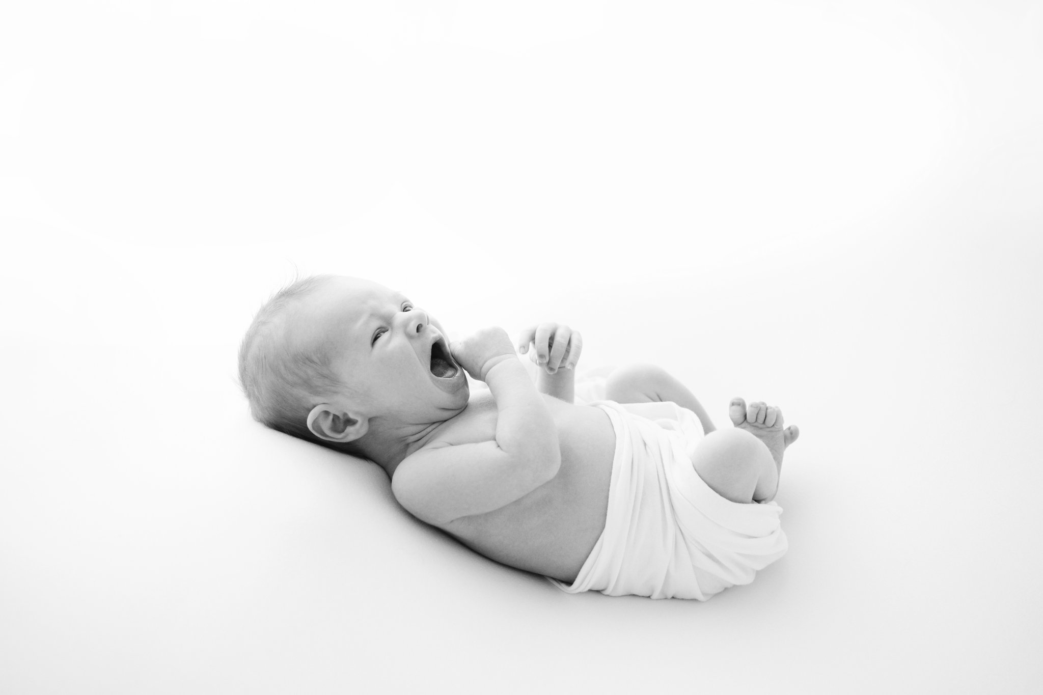 Newborn baby laying on back, yawning while being photographed in studio in Jupiter Fl
