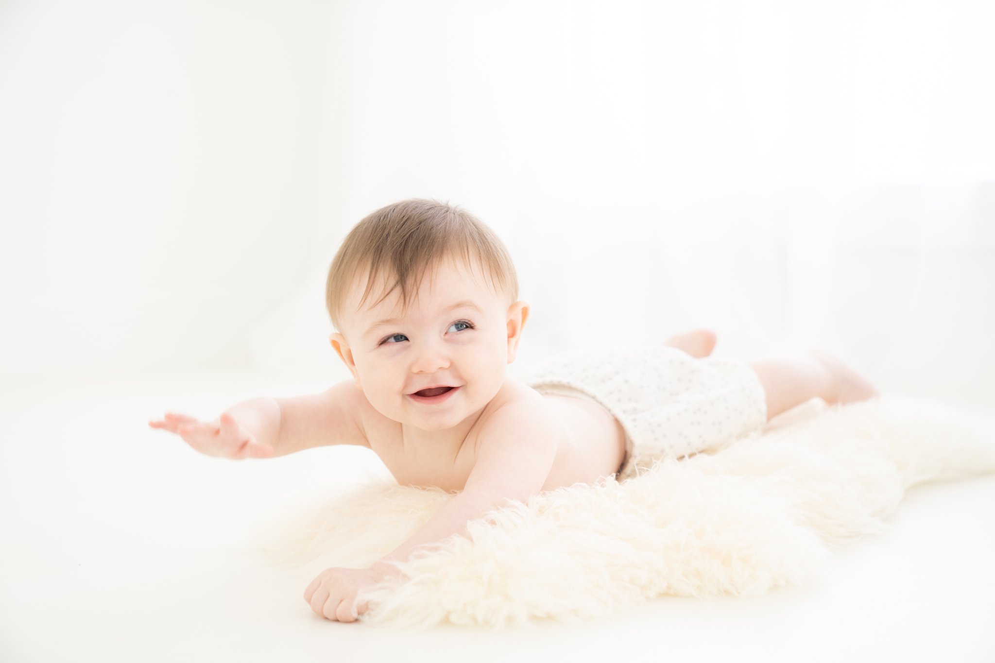 Baby boy laying of furry rug smiling while having his pictures taken in a Jupiter Fl photography Studio