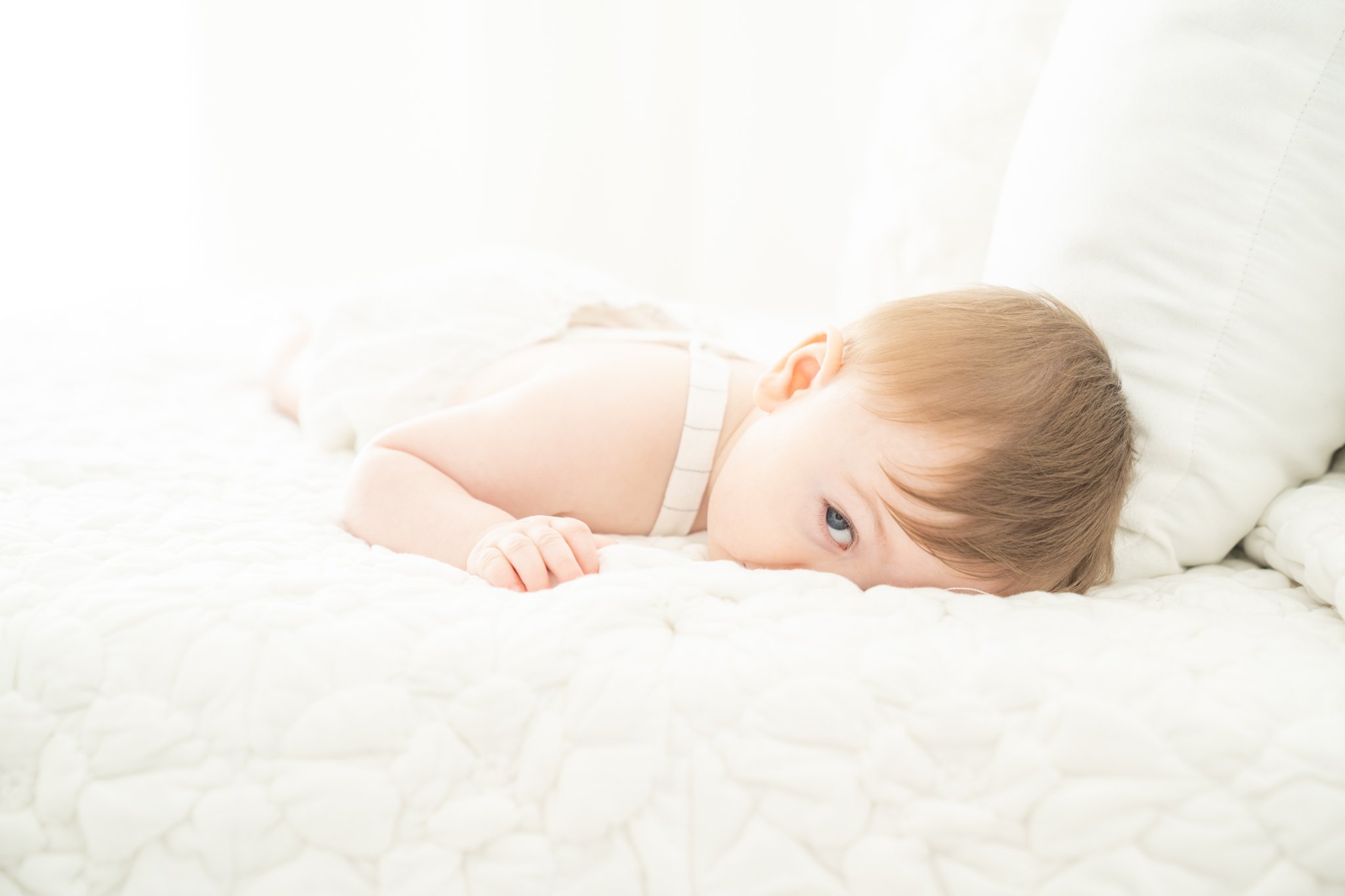 Baby boy lying on bed playing peek-a-boo in a Jupiter Fl photography Studio