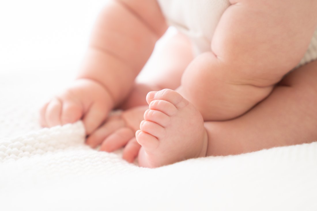 Baby photographer capturing baby boy playing with feet while laying on a white blanket