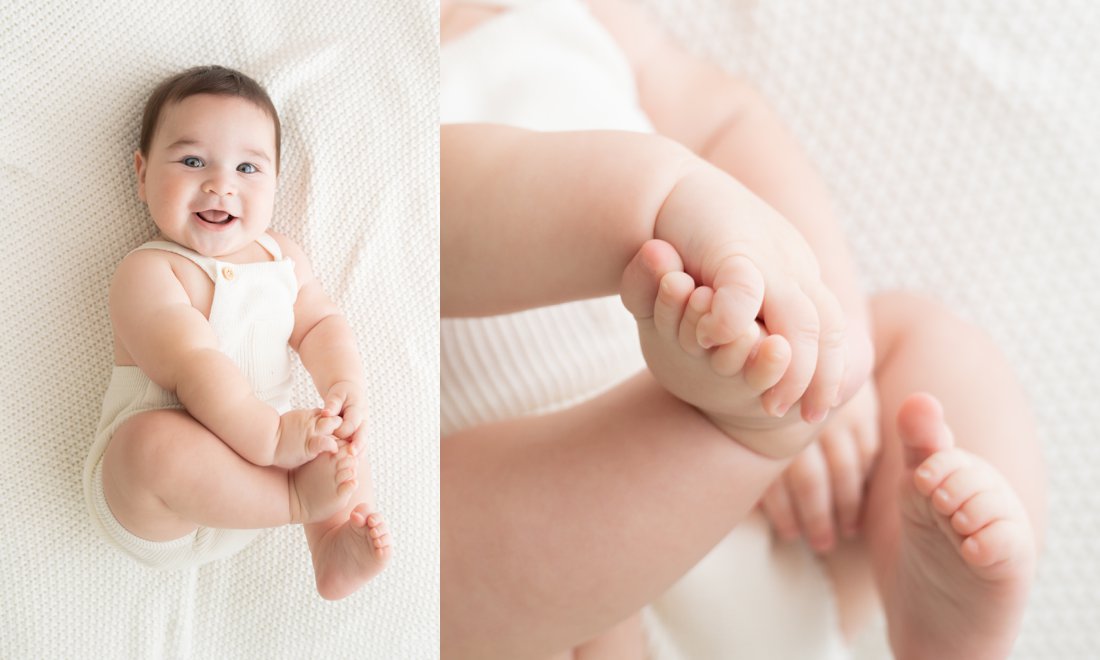 Baby photographer capturing baby boy playing with feet while laying on a white blanket