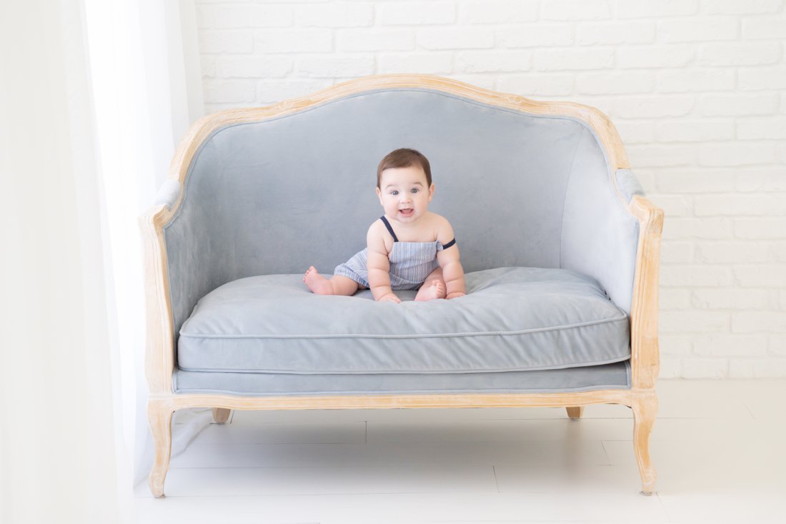 Baby boy sitting on a blue velvet settee in a photography studio in Jupiter Florida
