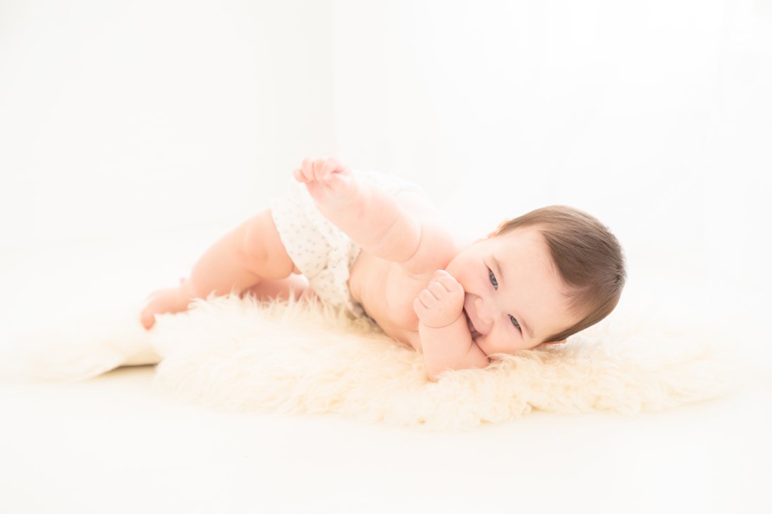  Photographer making baby smile while laying on his back on a fur rug