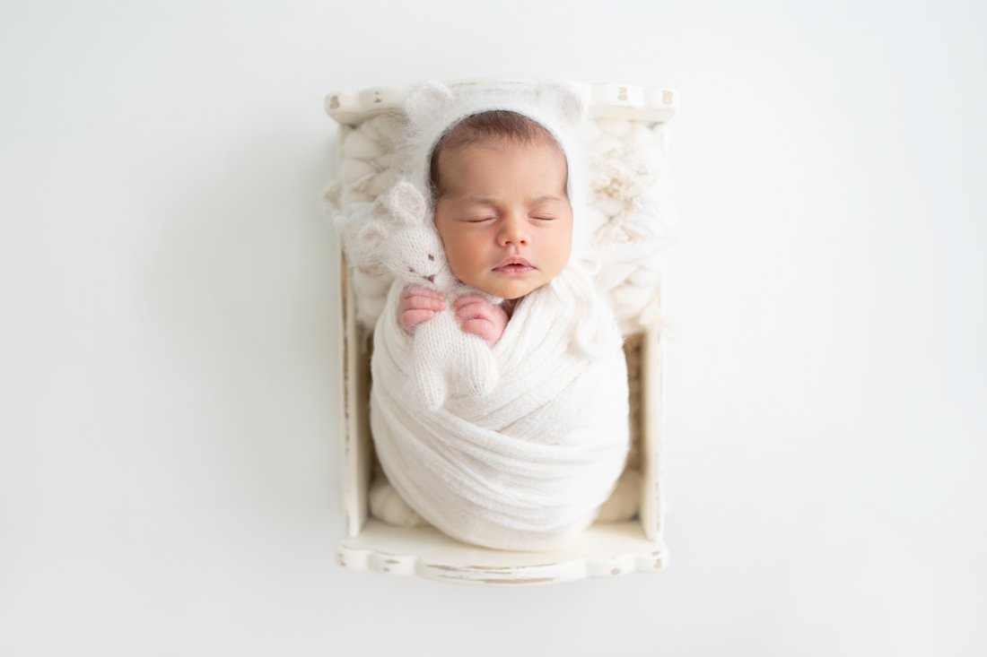 Newborn baby girl swaddled in a cream wrap lying in a newborn cradle prop 