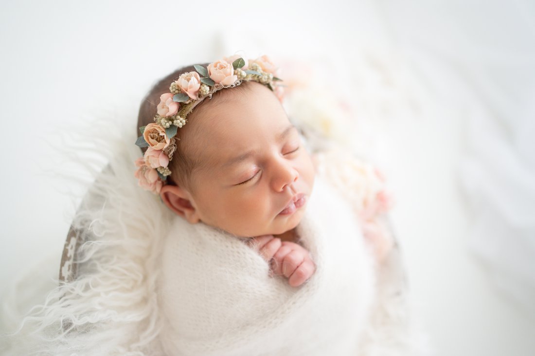 Newborn baby girl swaddled in a cream wrap lying in a bucket surrounded with peony flowers