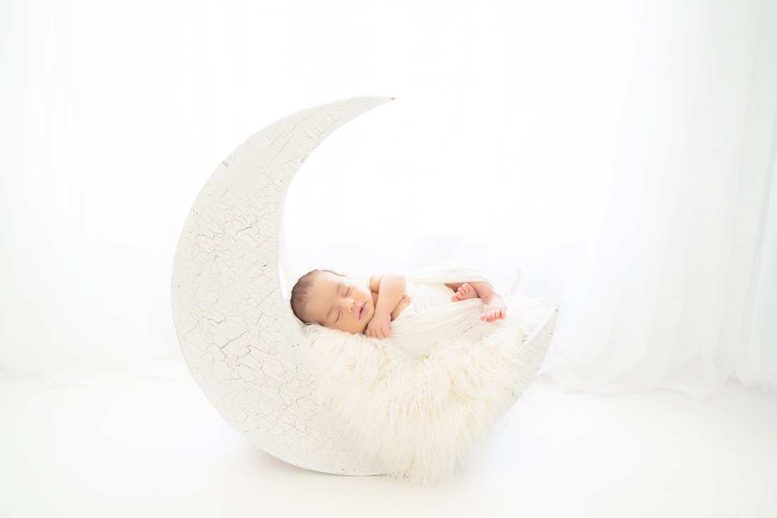 Newborn baby girl swaddled in a cream wrap lying a moon prop in jupiter photography studio