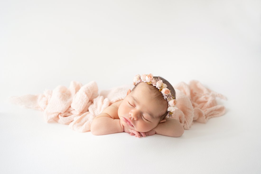 Newborn baby girl laying on her tummy with a pink flower halo on her head