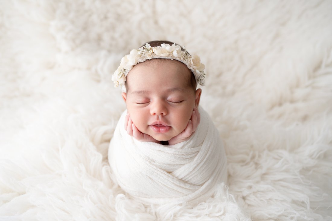 Newborn baby girl swaddled in a cream wrap with a cream flower halo on her head