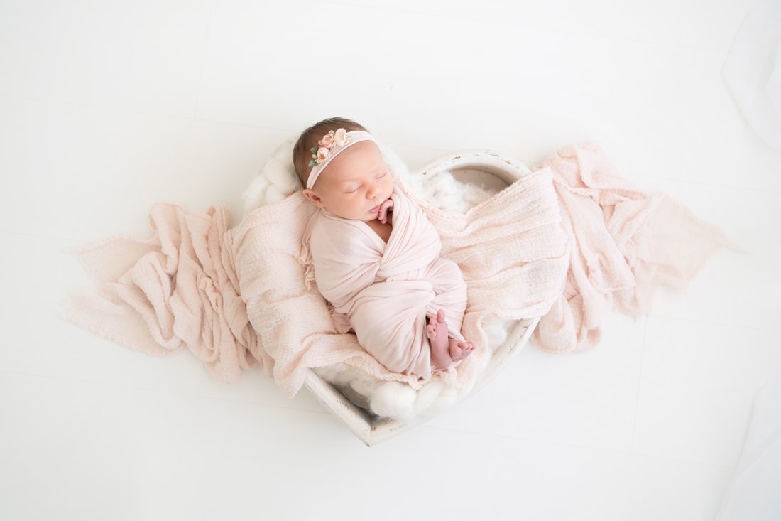 Newborn baby lying in a heart bowl swaddled in pink