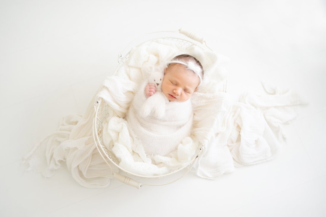 Newborn baby swaddled in a cream wrap lying in a wire basket