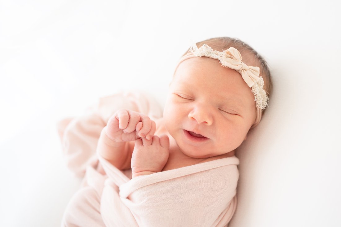 Newborn baby swaddled in a pink wrap lying on her back wearing a pink headband bow