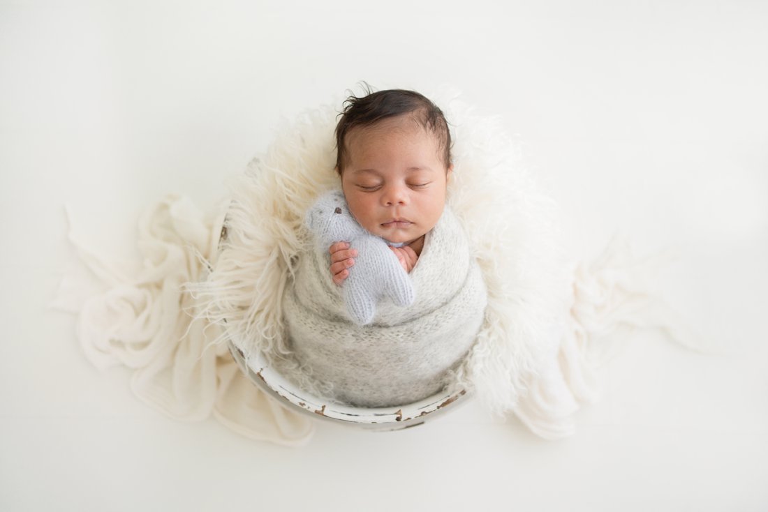 Newborn baby boy lying in a bucket being photographed in a natural light studio