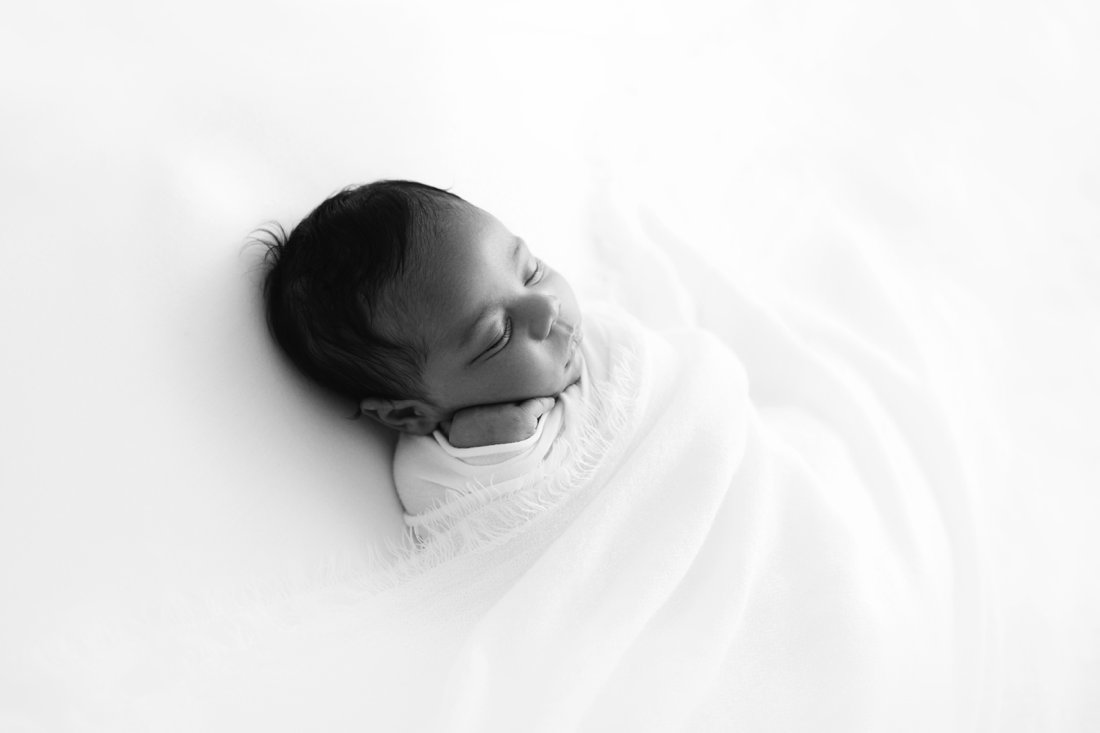 Newborn baby wrapped in white lying on his back