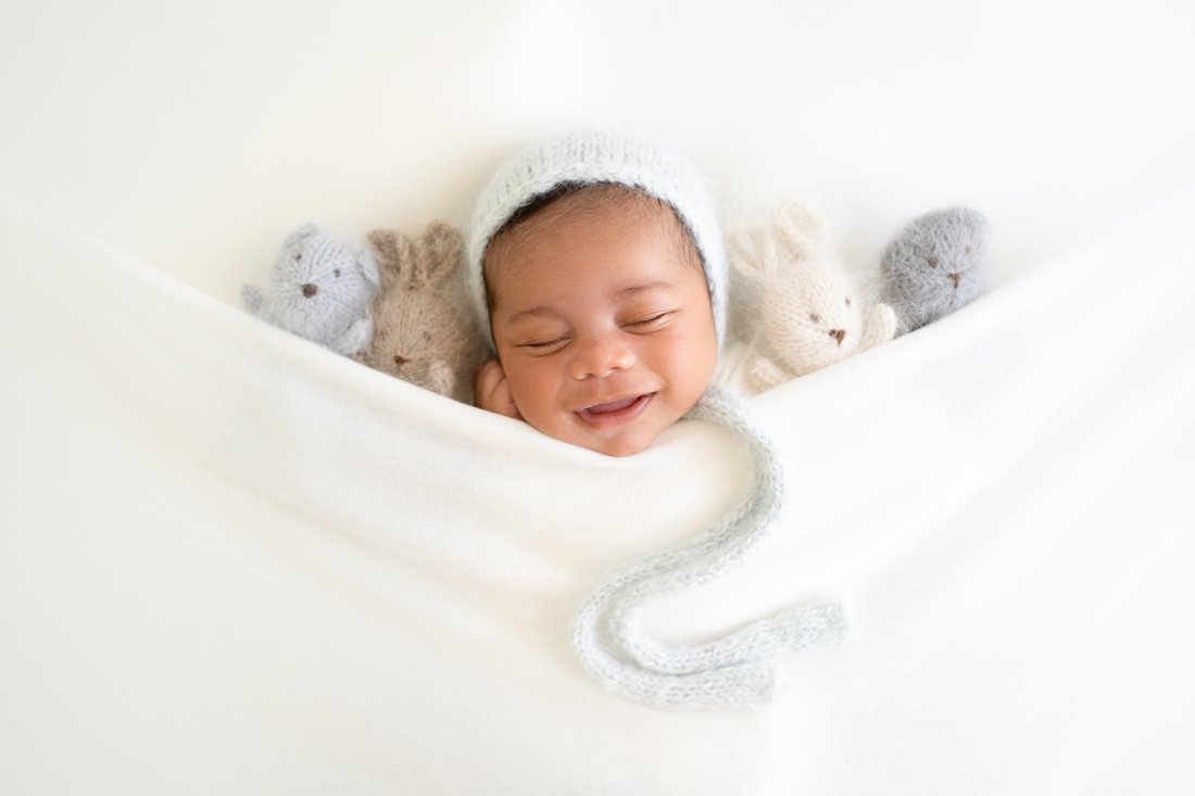 Newborn baby lying tucked in with teddy bears and bunny rabbits