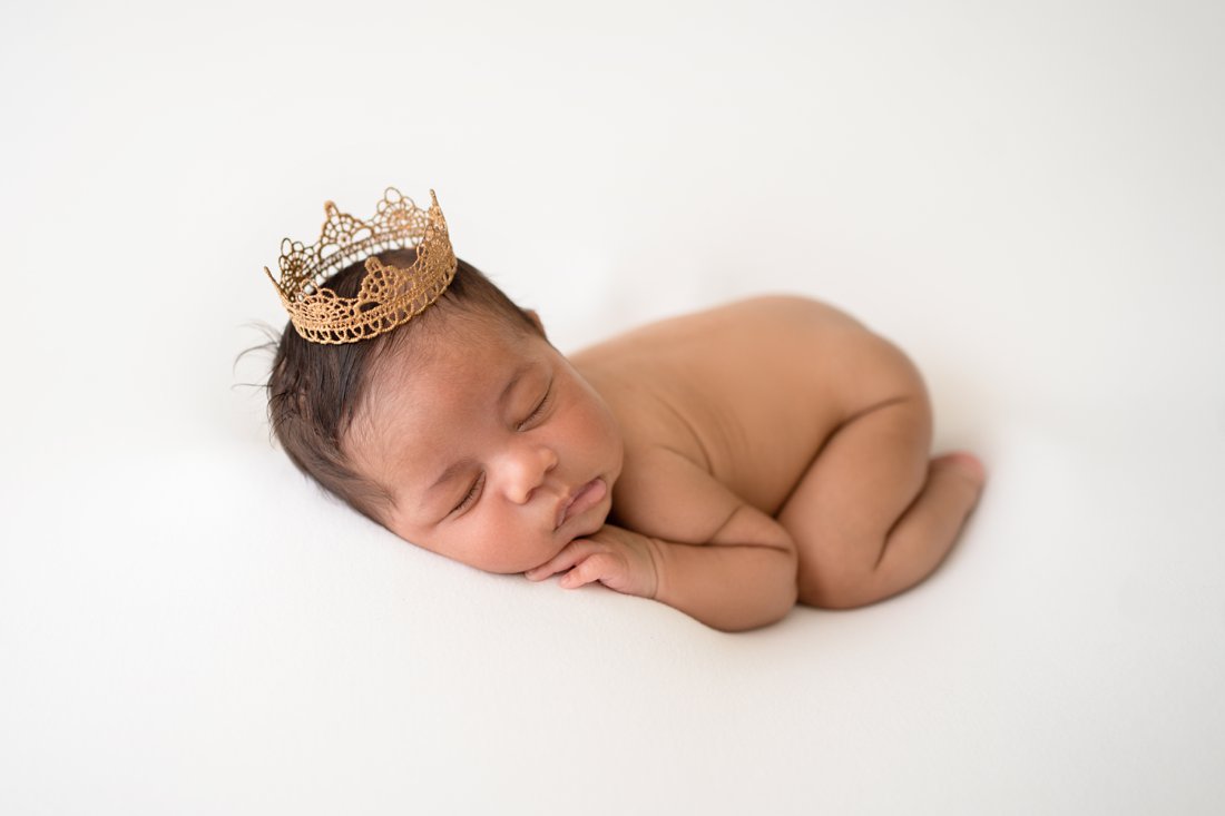 Newborn baby boy lying on his tummy wearing a prince's crown
