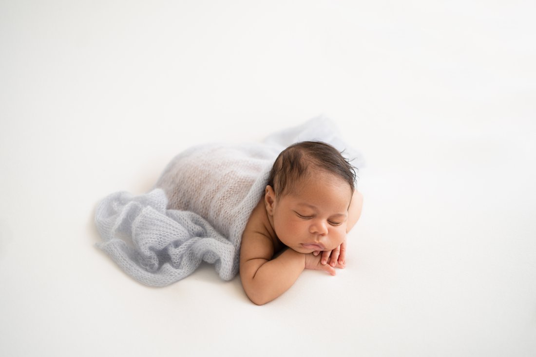 Newborn baby boy lying on his tummy with blue wrap drapped over his back
