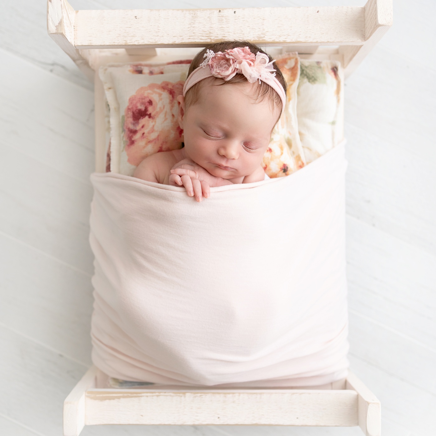  newborn baby on a pink bed with a floral pillow