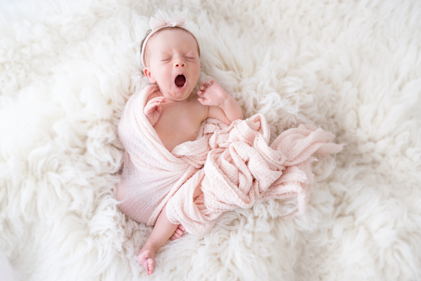  newborn baby girl wrapped in pink laying on a fur backdrop