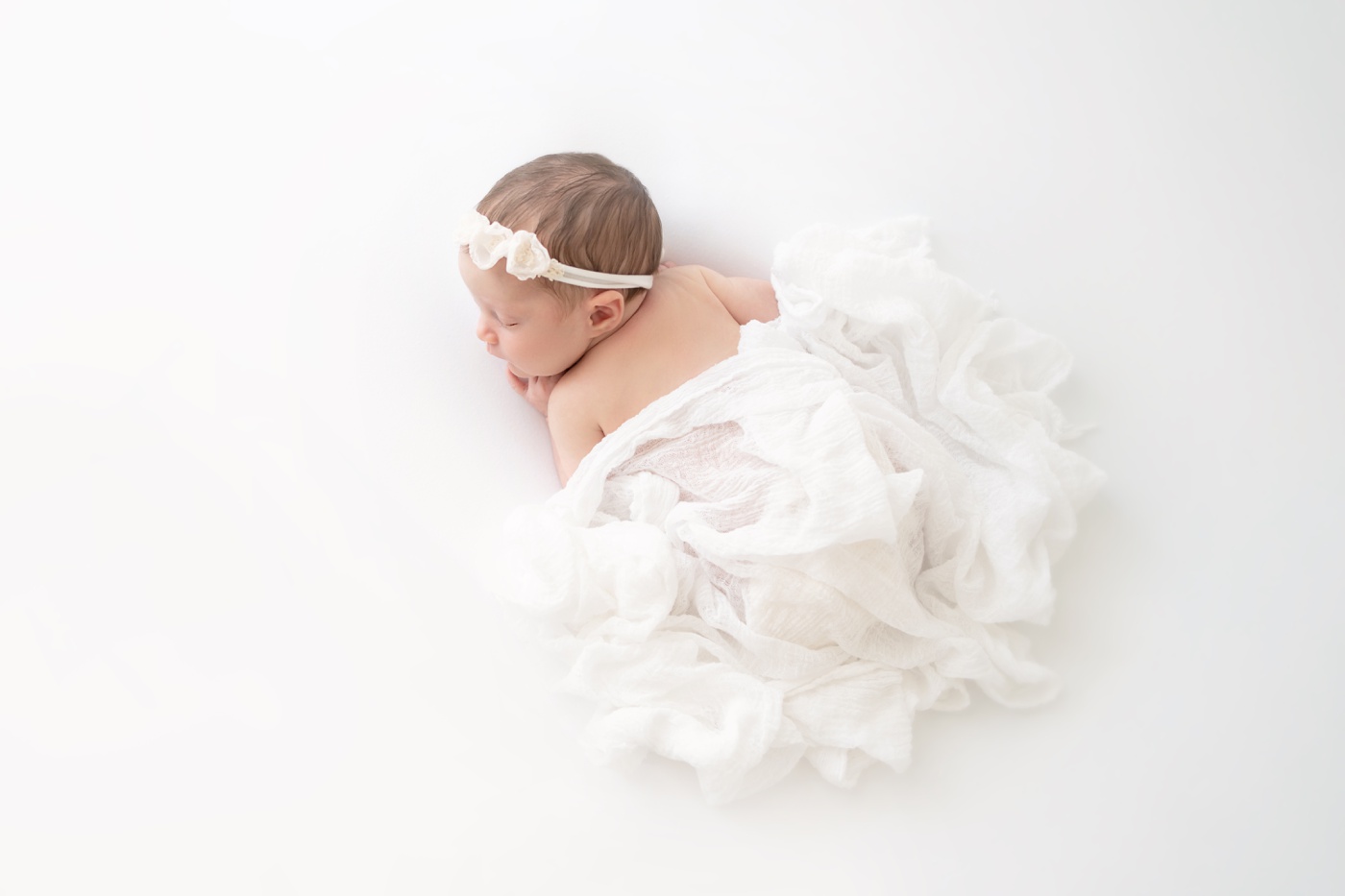  newborn baby on white bacdrop with white wrap draped over her back