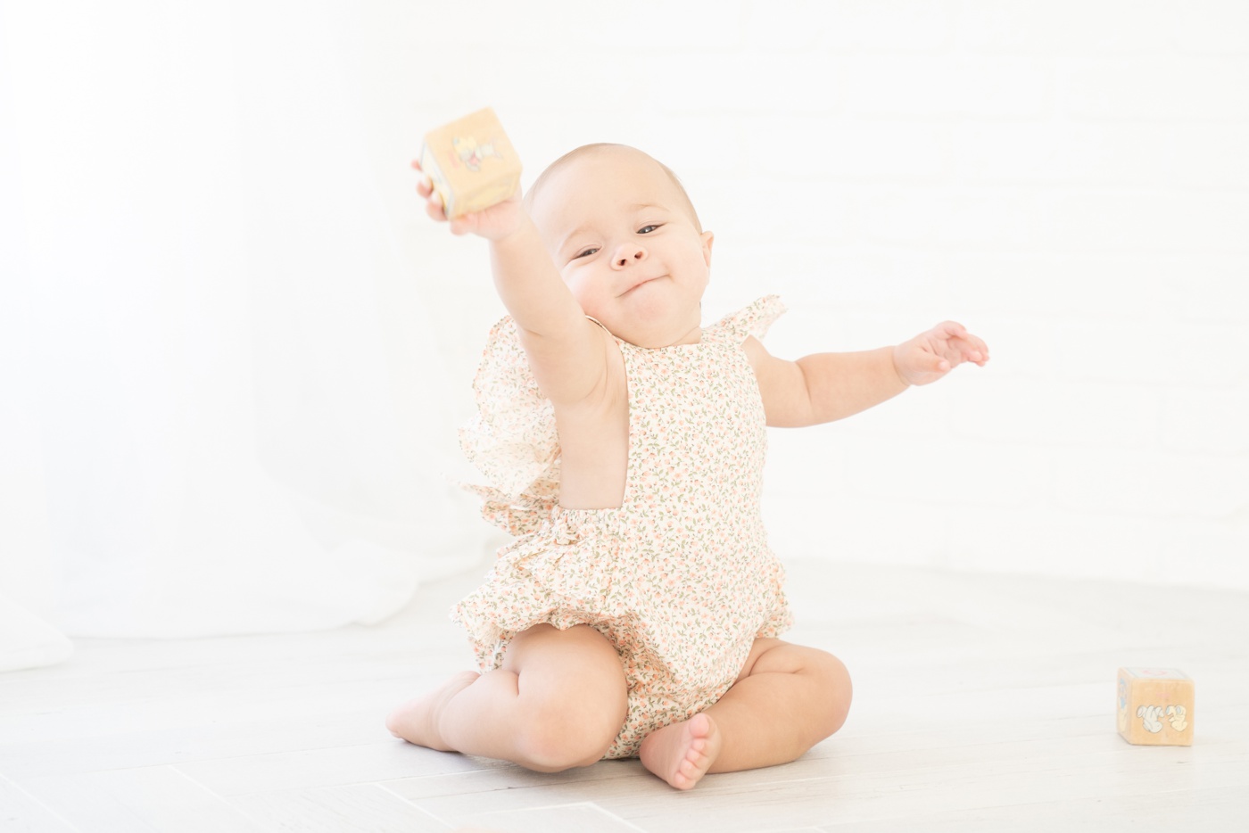 Baby ia floral romper being photographed in an all white Jupiter Fl photo studio playing with wooden blocks