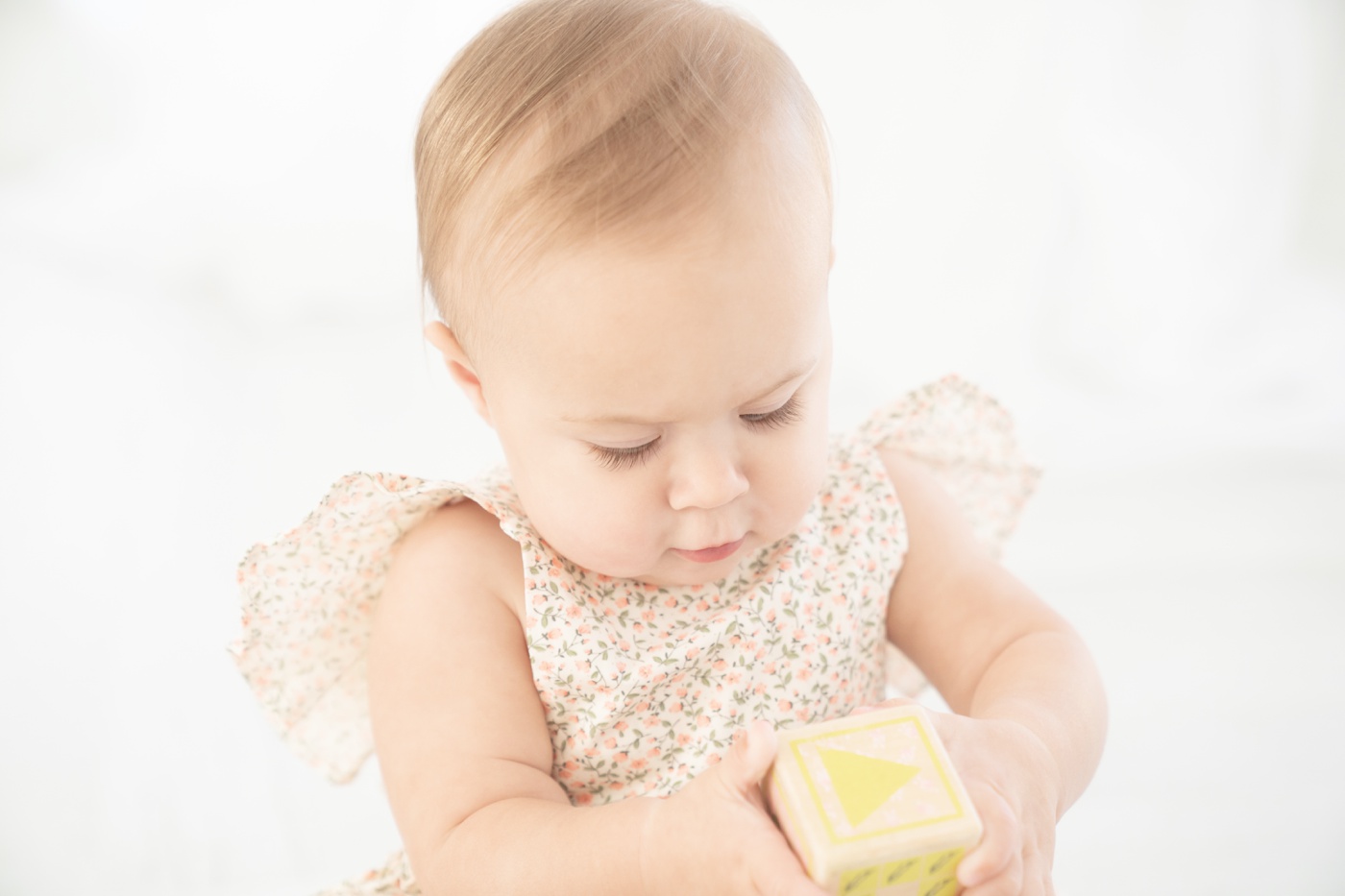Baby ia floral romper being photographed in an all white Jupiter Fl photo studio playing with wooden blocks