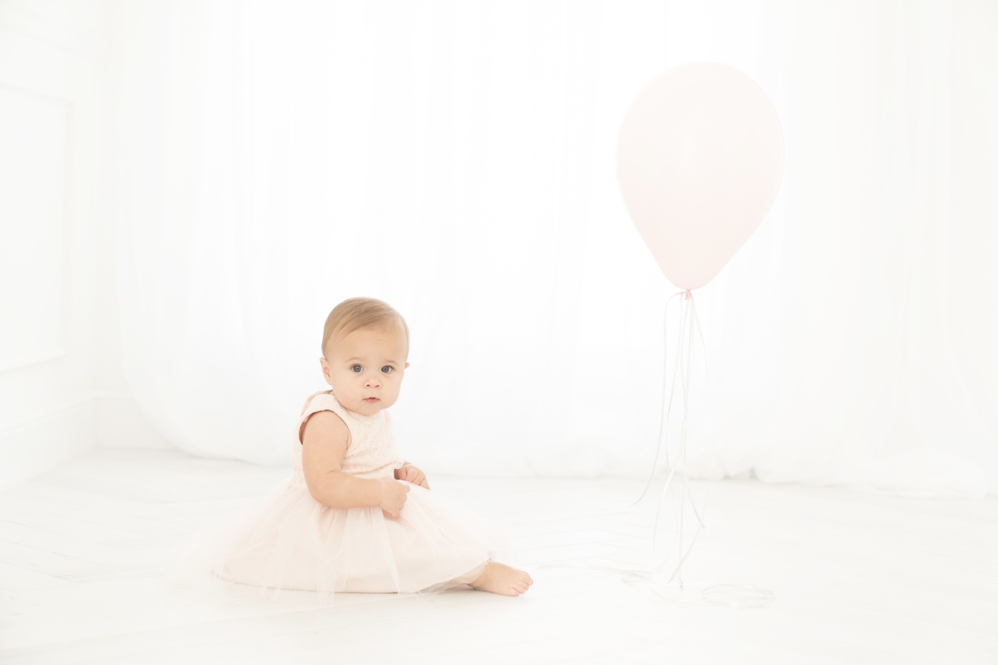 Baby ia in a pink dress with her one year birthday balloon