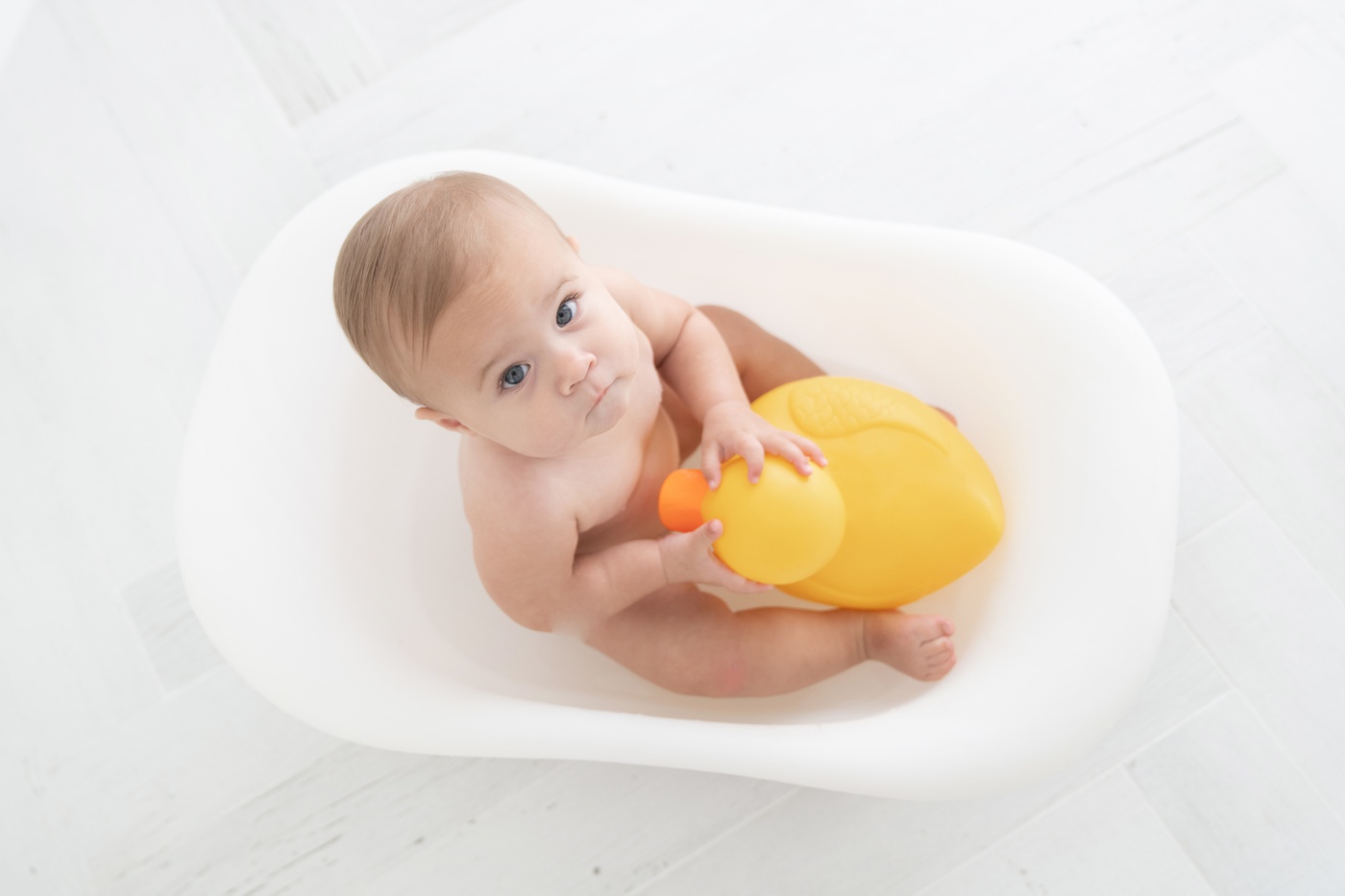 Baby girl in a in tiny white bathtub by a natural light window being photographed for her one year photoshoot