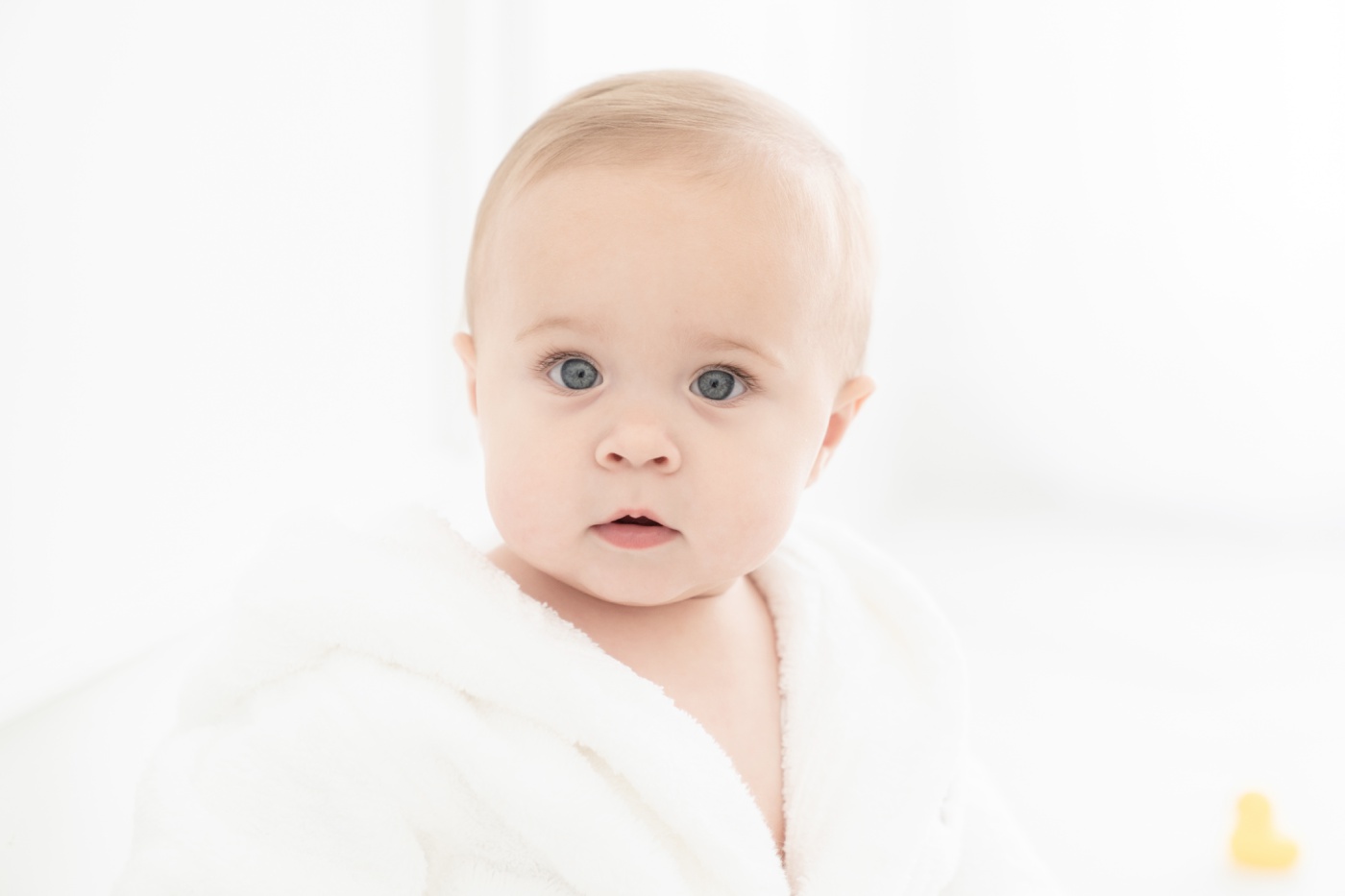 Baby girl in a white bathrobe by a natural light window being photographed for her one year photoshoot