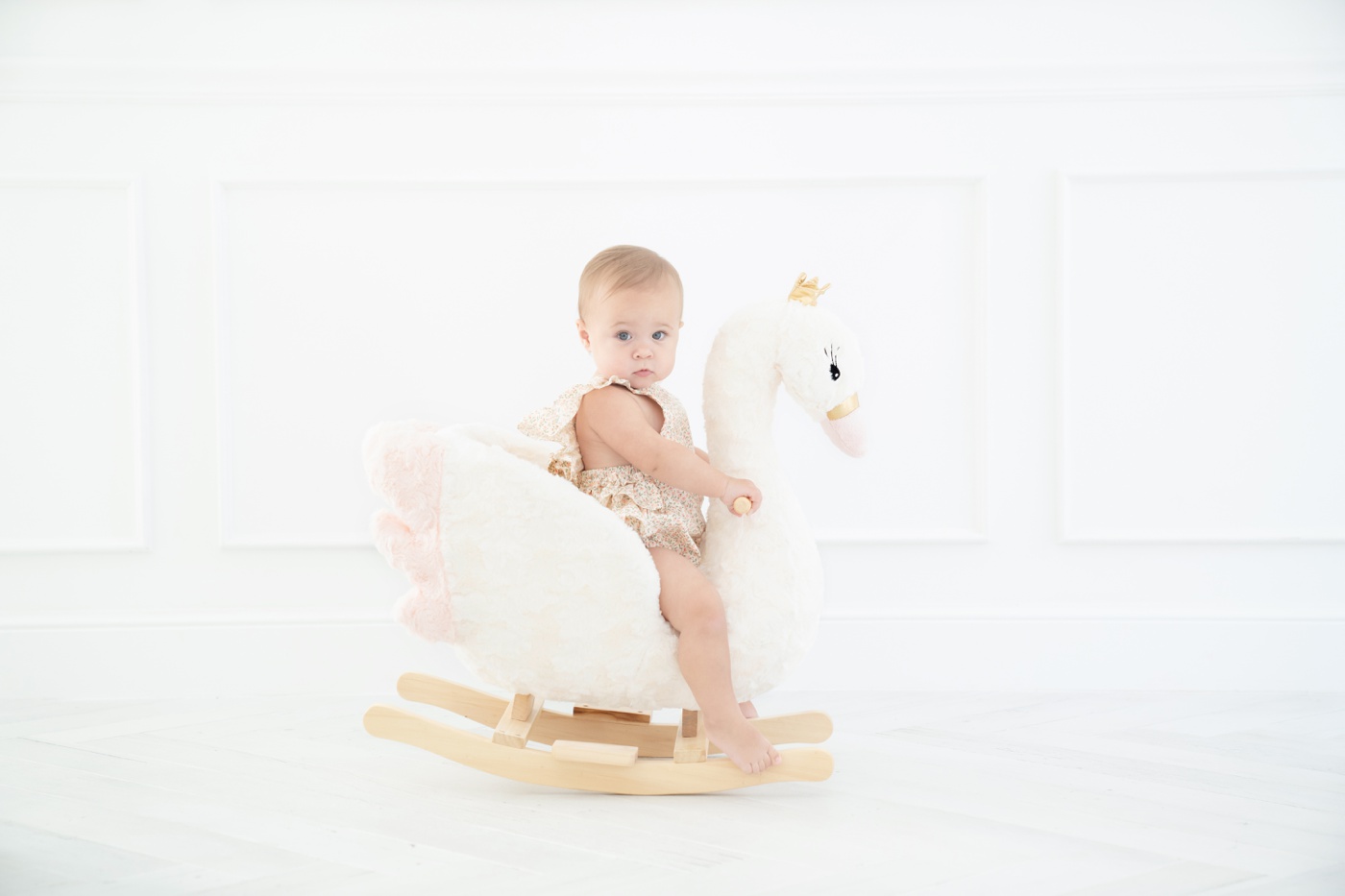 Baby ia floral romper sitting on a swan rocker in an all white Jupiter Fl photo studio