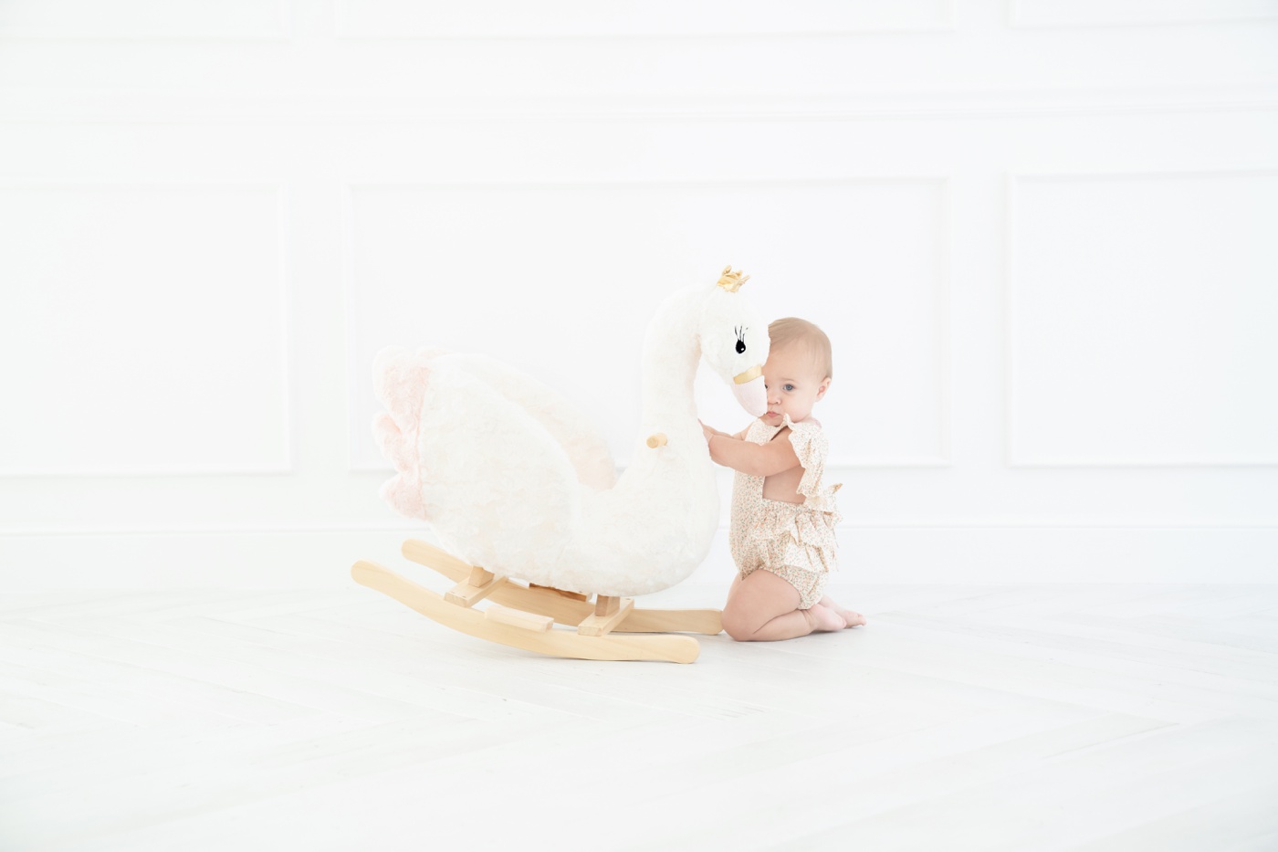 Baby ia floral romper sitting on a swan rocker in an all white Jupiter Fl photo studio