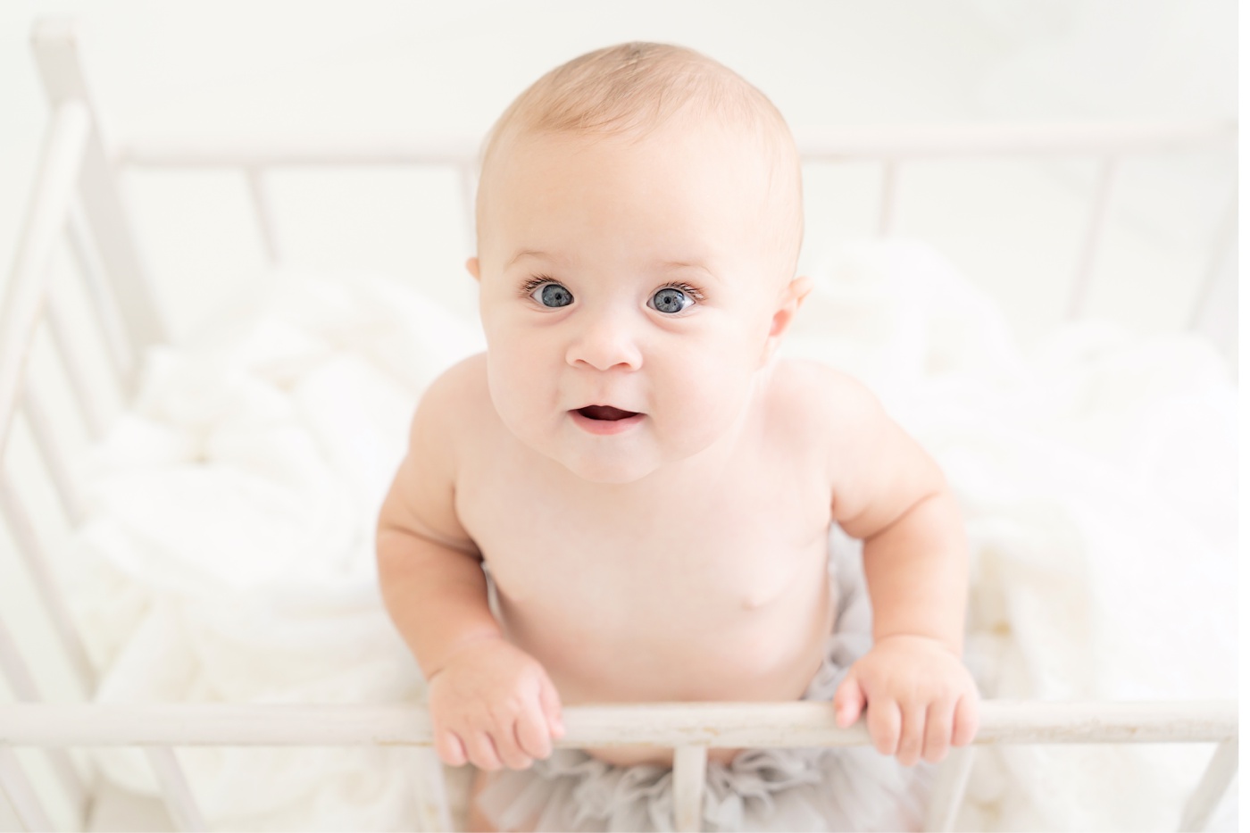 baby in antique crib being photographed in a white photography studio
