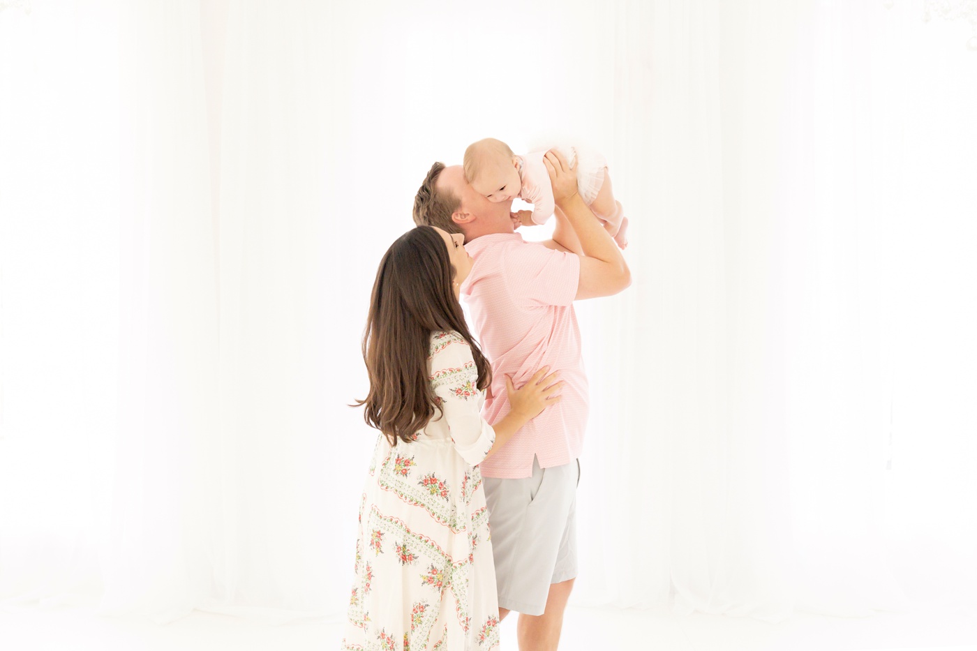 Mom, Dad and baby being photographed in a white photography studio