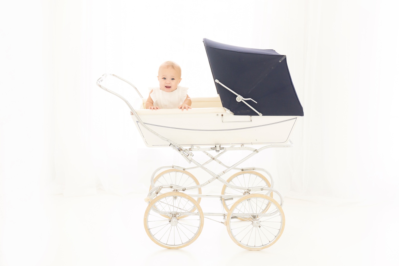 baby and antique vintage white pram being photographed in a white photography studio