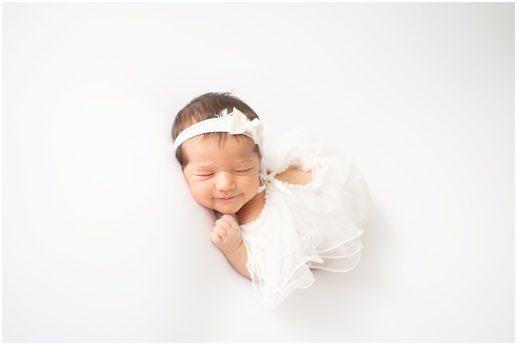 New baby at her first Newborn photoshoots wearing a while baby outfit with pearls.