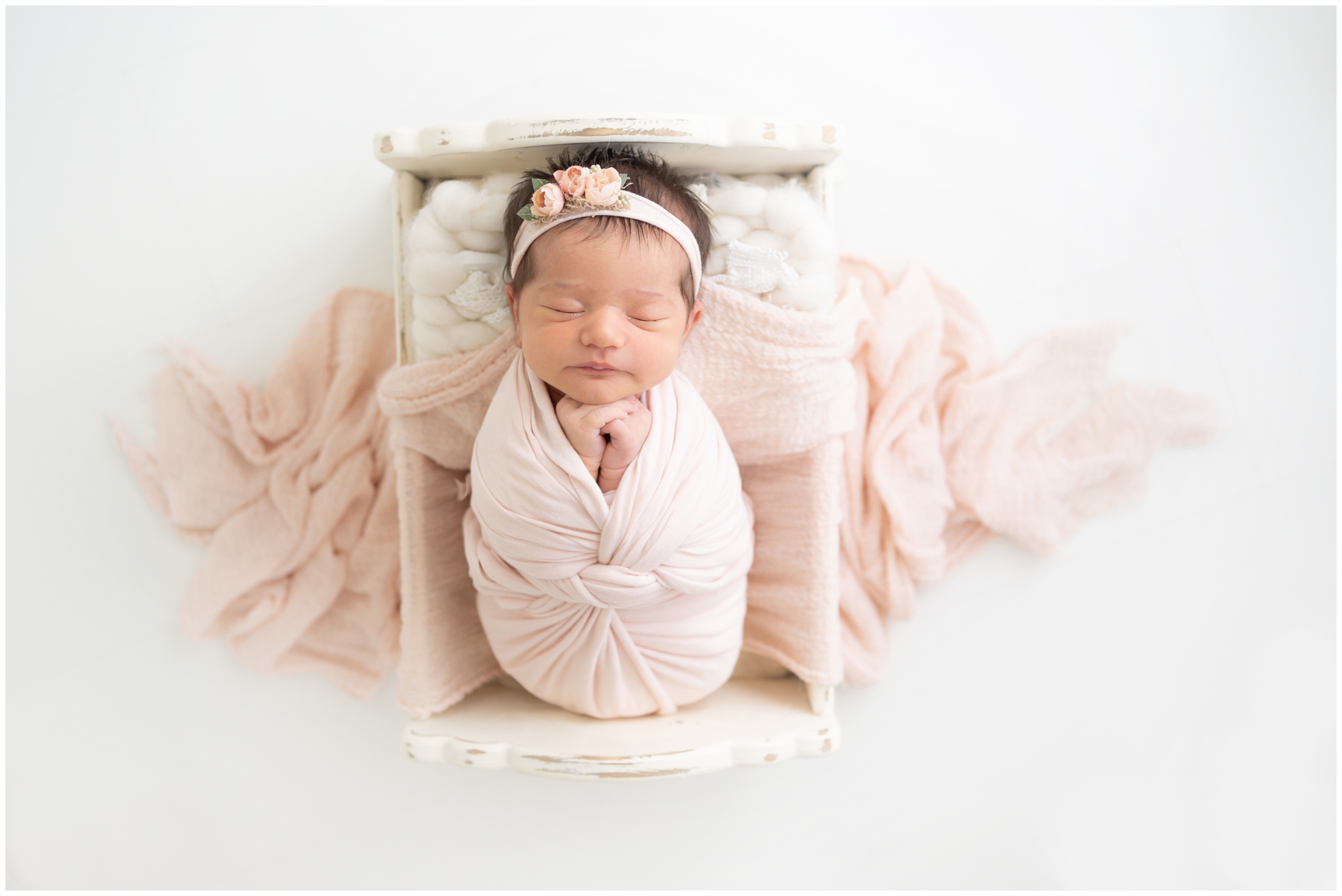 Brand new baby swaddled in pink laing in a cradle being photographed in Jupiter Fl studio