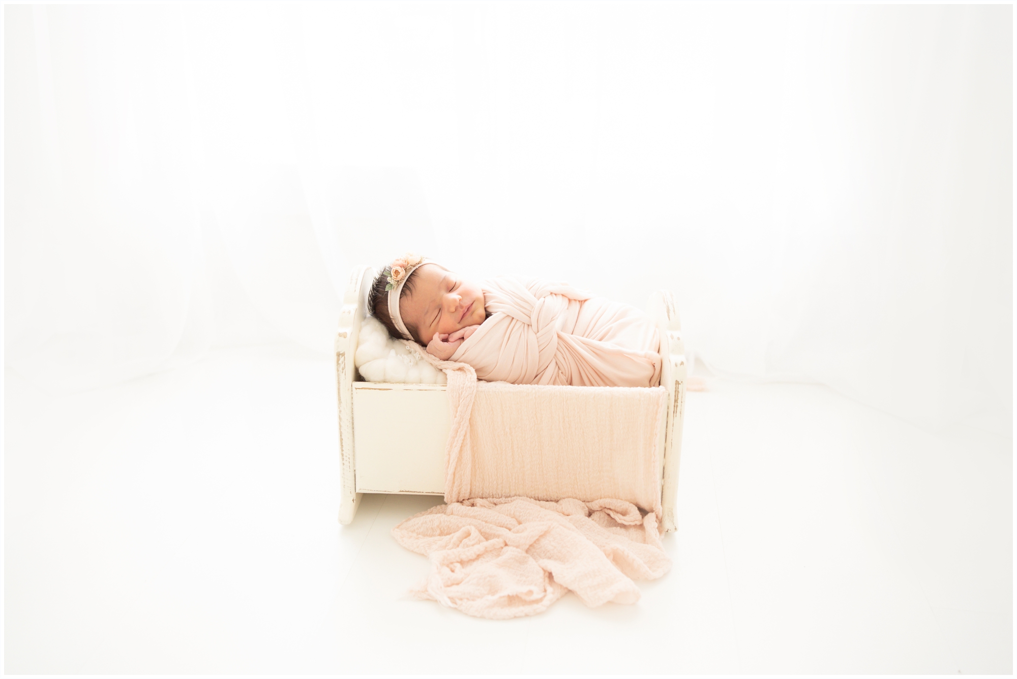 Brand new baby swaddled in pink laing in a cradle being photographed in Jupiter Fl studio