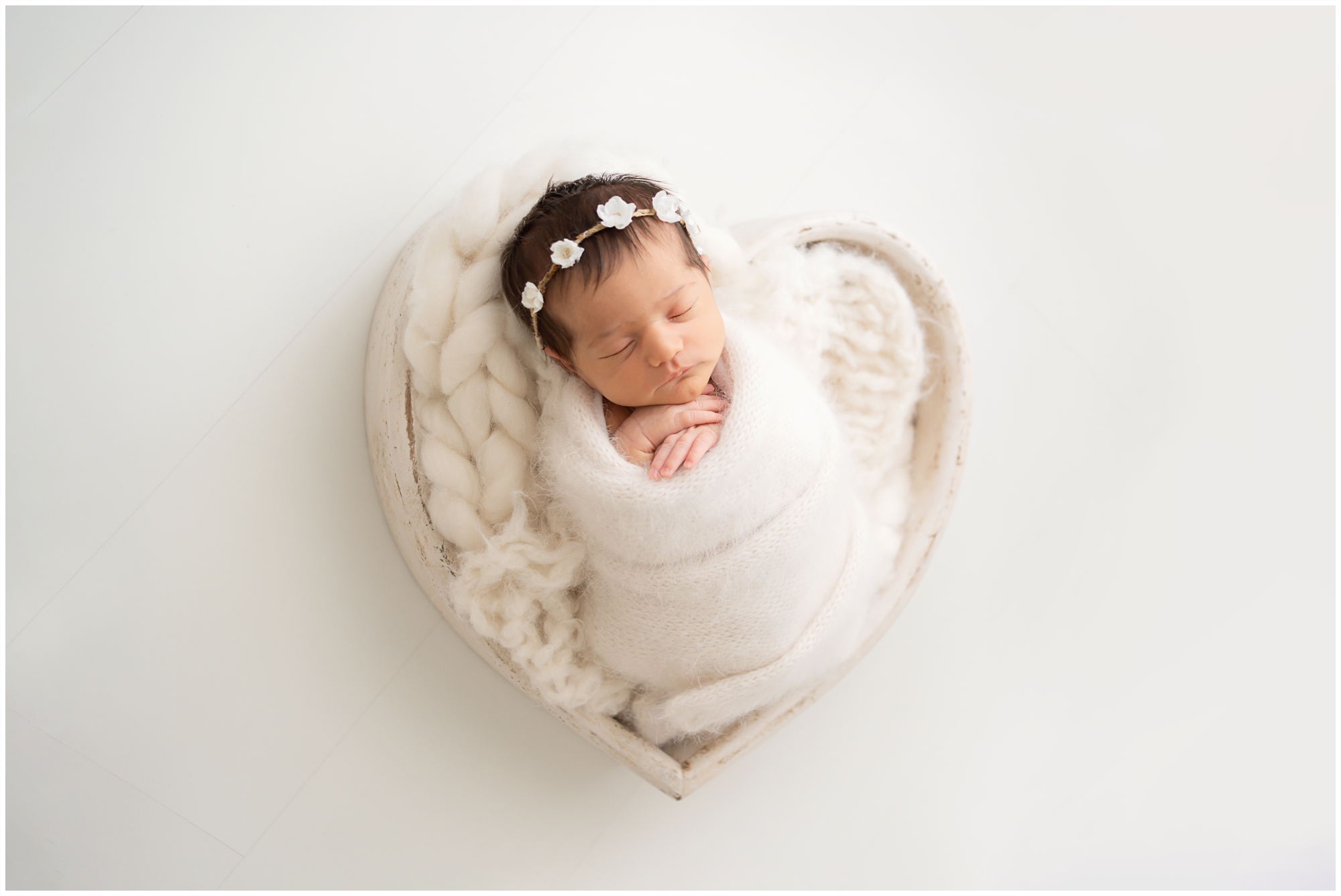 Brand new baby swaddled in white laying in a heart shaped bowl being photographed in Jupiter Fl studio