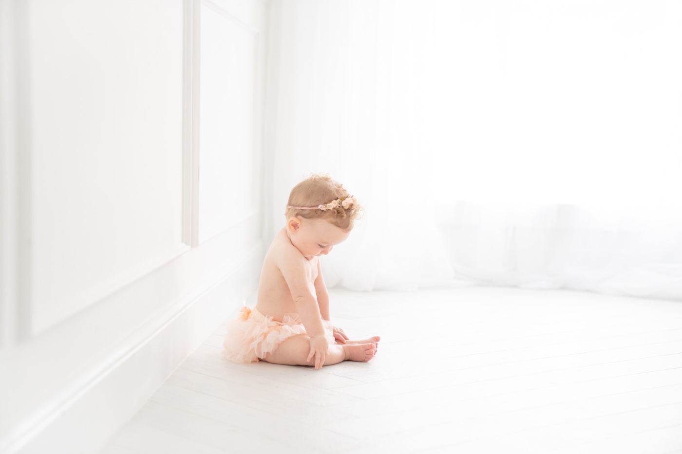 Baby girl sitting in on the floor in a peach tutu having her sitter milestone photos taken