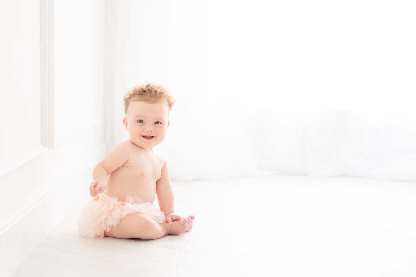 Baby girl sitting in on the floor in a peach tutu having her sitter milestone photos taken