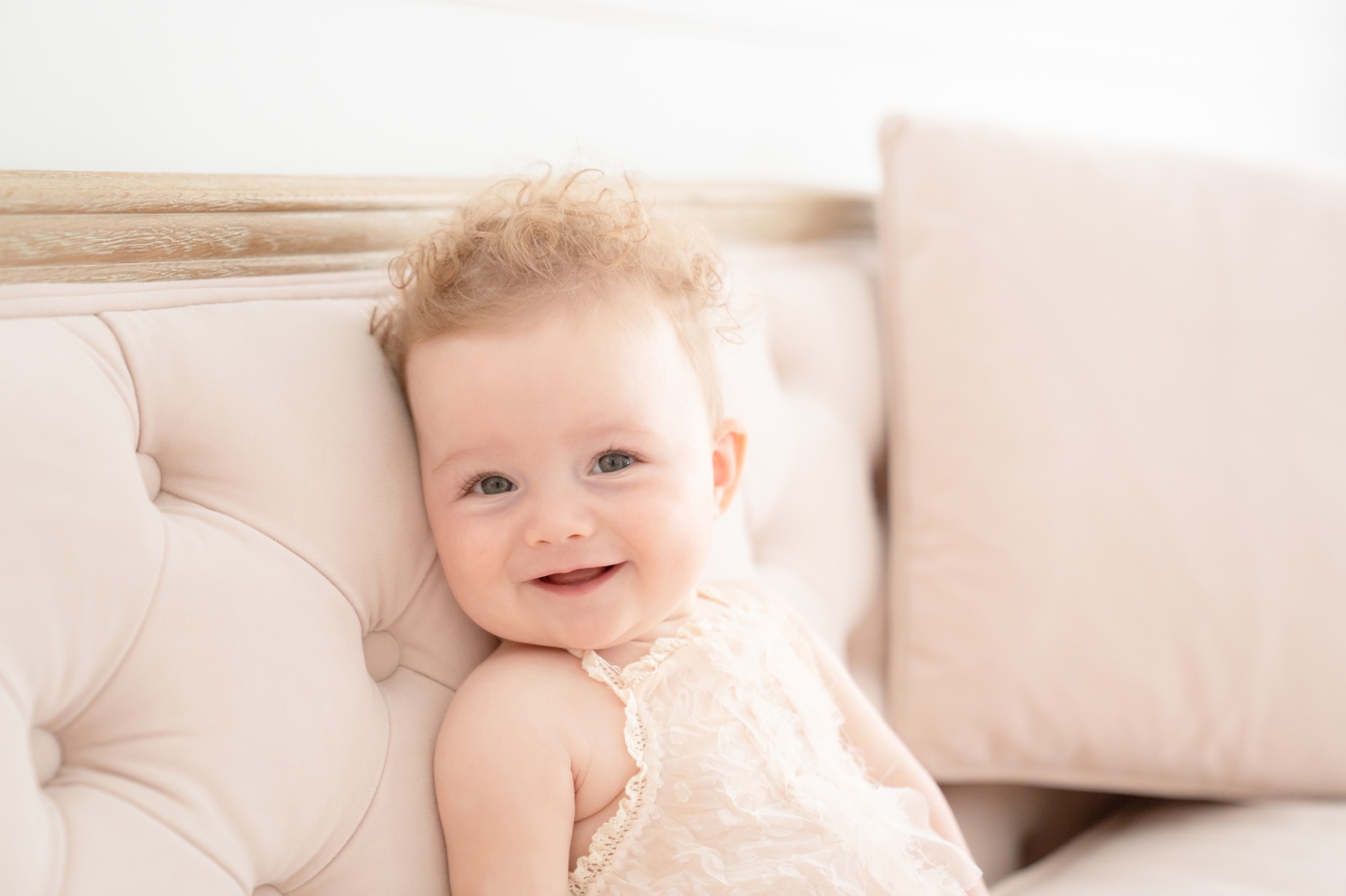 Baby girl sitting on a pink couch in an all white photo studio