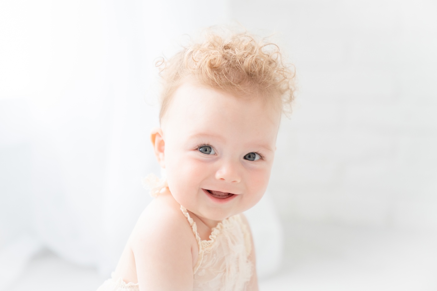 Baby girl sitting on the floor of an all white photo studio