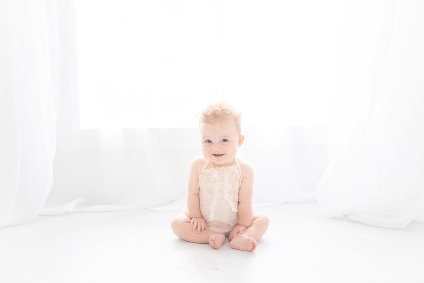 Baby girl sitting on the floor of an all white photo studio