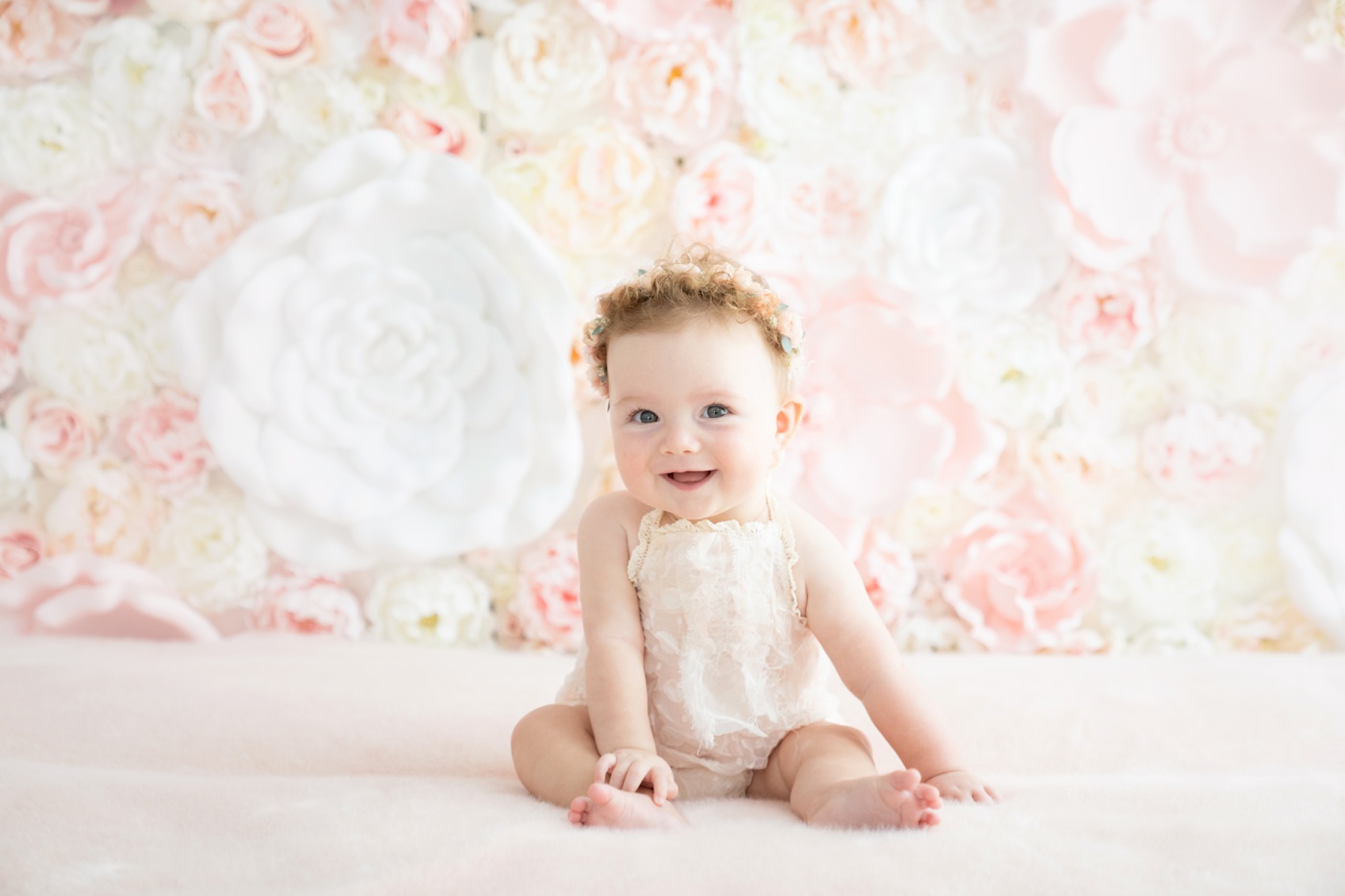 Baby girl sitting in front of a pink and white flower wall